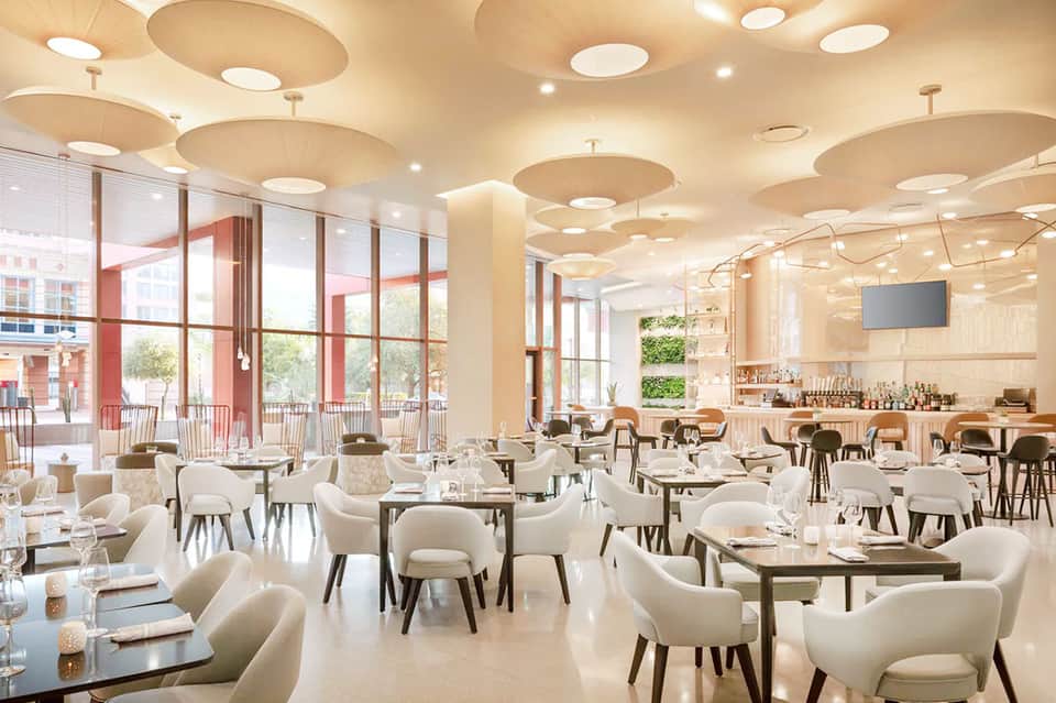 Contemporary restaurant dining room with white chairs, circular ceiling details, and large windows