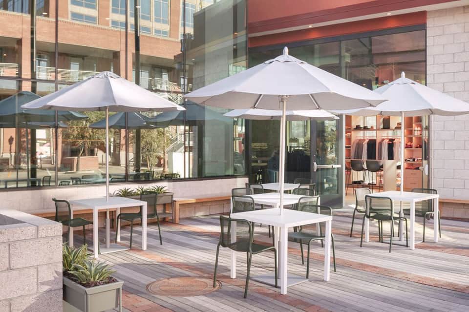Outdoor terrace with white umbrellas, tables, chairs, and modern building facade in daylight