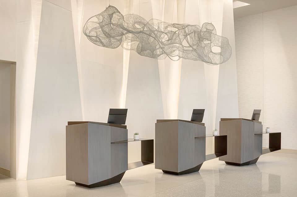 Modern hotel lobby with minimalist reception desks and hanging wire sculpture artwork