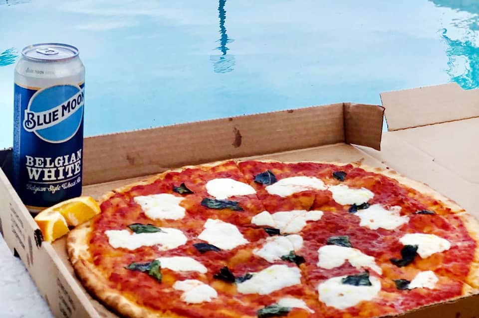 Margherita pizza with mozzarella and basil beside Blue Moon beer can at poolside
