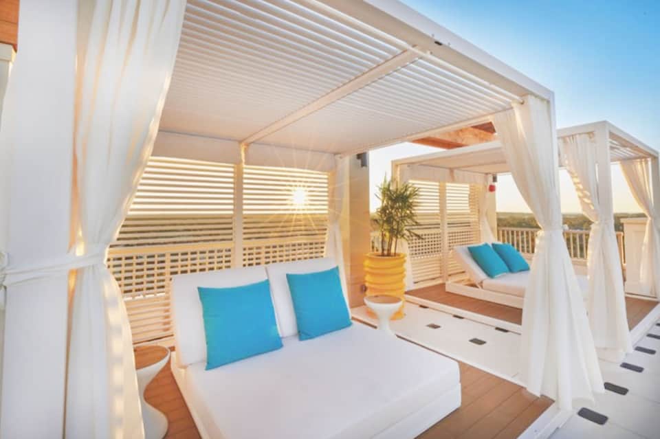 White cabana beds with blue pillows on oceanview deck with louvered shade structure