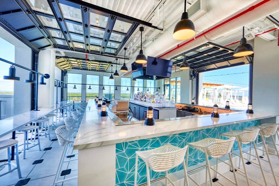 Modern resort bar and lounge with blue and white accents, glass ceiling, and ocean views
