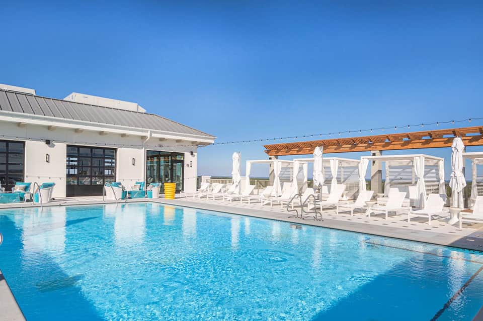 Resort outdoor pool with white loungers and pergola structure under clear blue sky