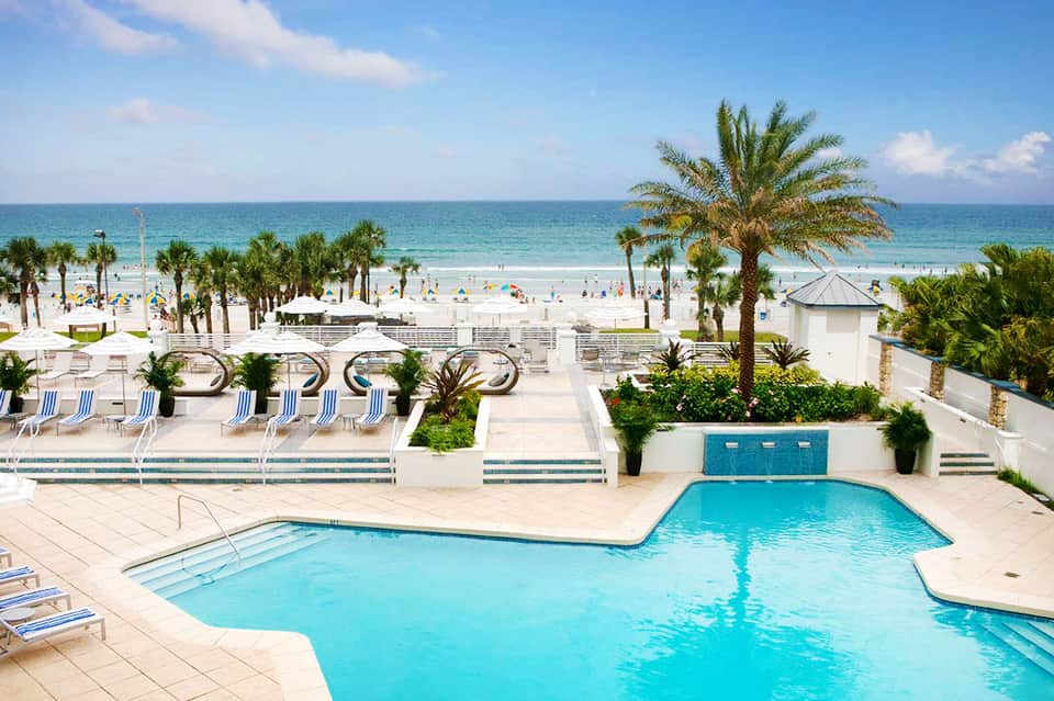 Resort pool deck with loungers, palm trees, and beach access beyond