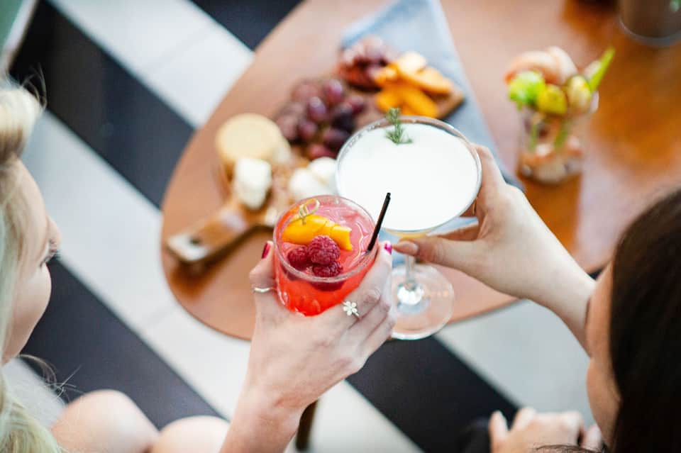 Woman holding colorful cocktails at resort gathering with charcuterie board background