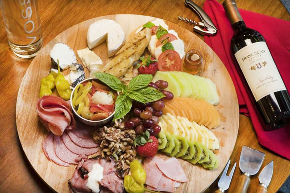 Charcuterie board with cured meats, cheeses, fruits, and wine bottle on table