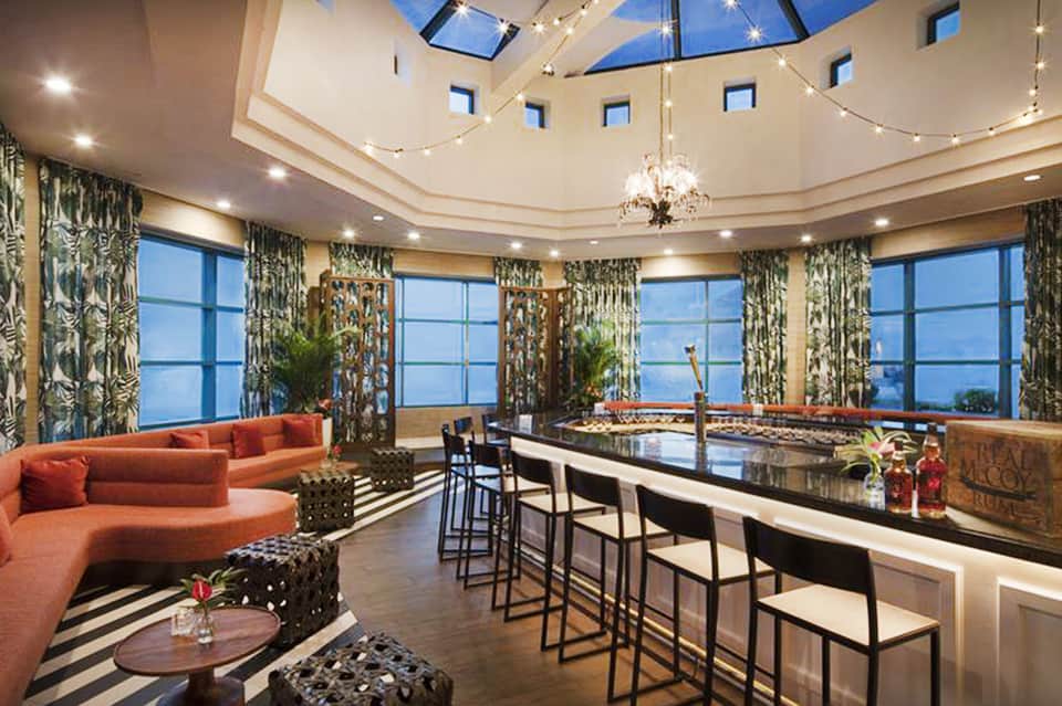 Luxury penthouse living room with curved orange sectional, panoramic windows, and skylight ceiling