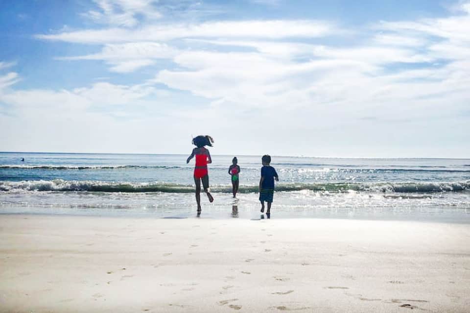 Family running into ocean waves on sandy beach under blue sky