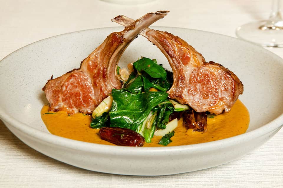 Plated lamb chops with sautéed greens and orange sauce on white ceramic dish