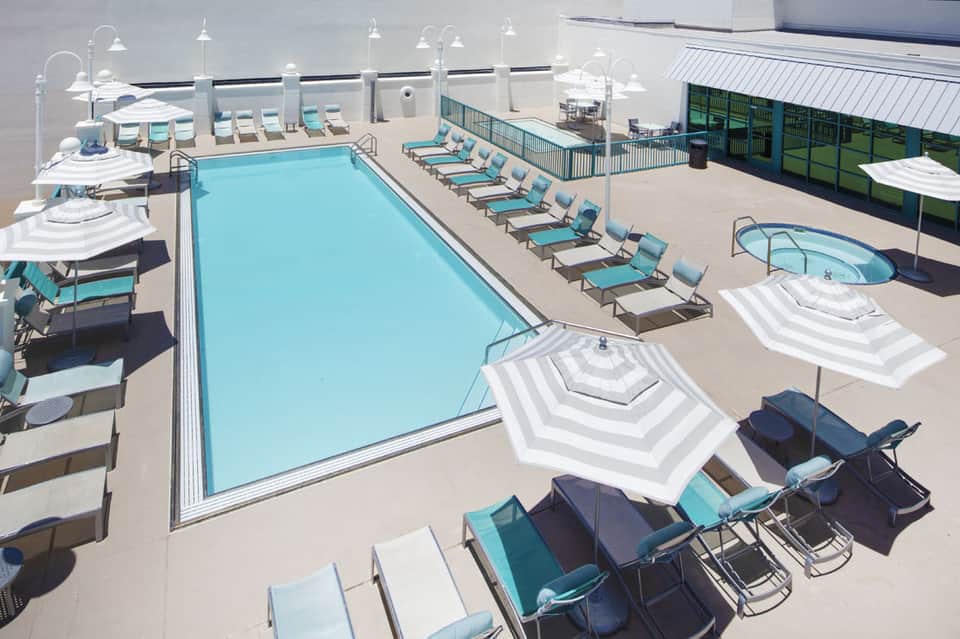 Aerial view of resort pool complex with lounge chairs, umbrellas, hot tub, and surrounding facilities