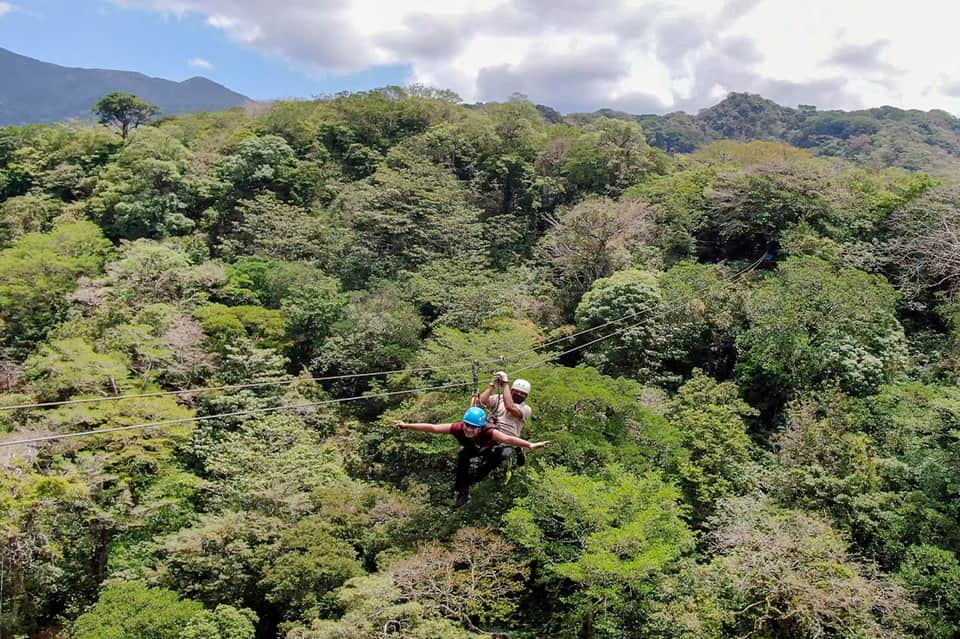 Person zip-lining through lush green rainforest canopy over mountains
