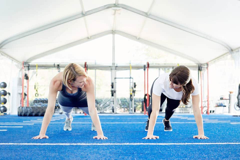 Two women exercising in a bright tent-covered fitness studio with equipment