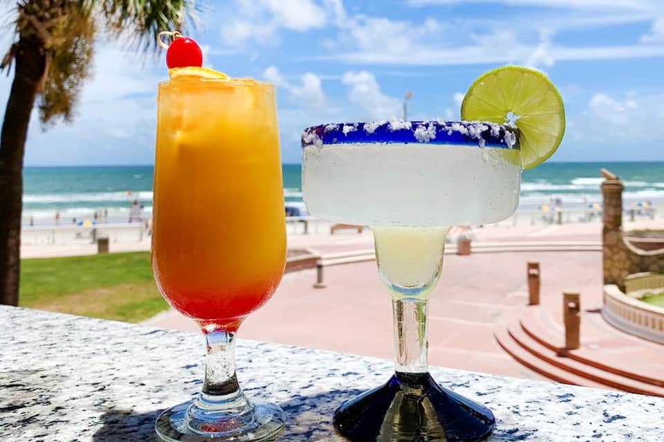 Tropical beach cocktails with ocean and sandy beach backdrop, including mai tai and margarita with salt rim