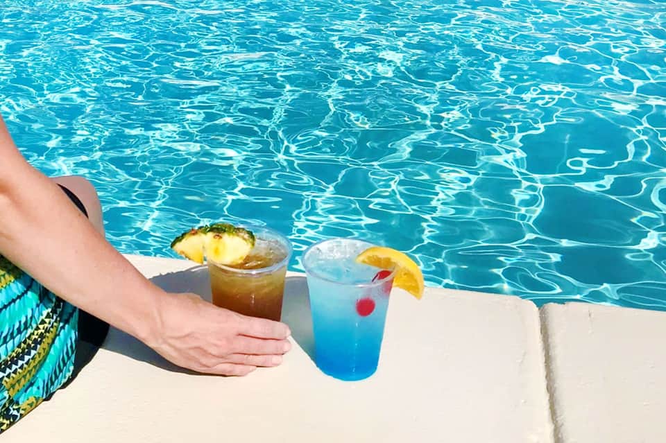 Poolside cocktails with tropical fruit garnishes on concrete deck overlooking bright blue water