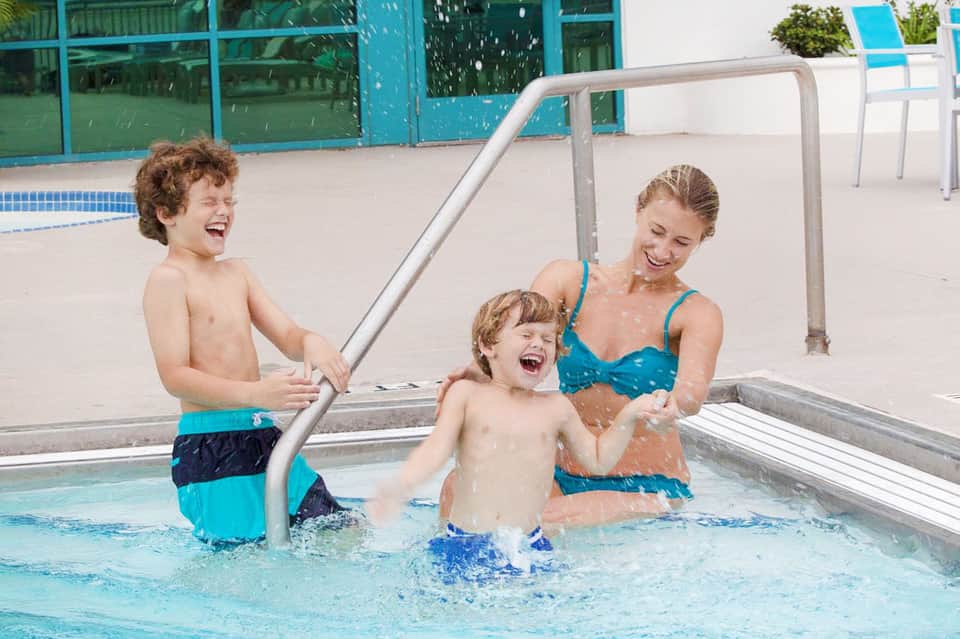 Young children playing in shallow outdoor pool with adult supervision