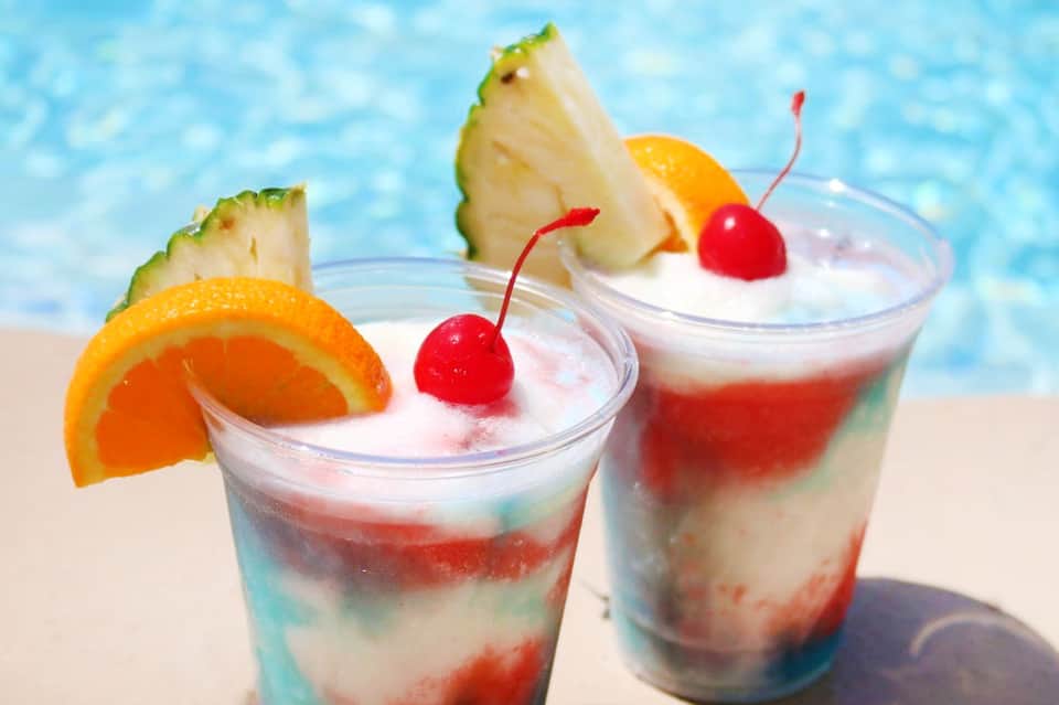 Tropical cocktails with fruit garnishes on beach sand by ocean water