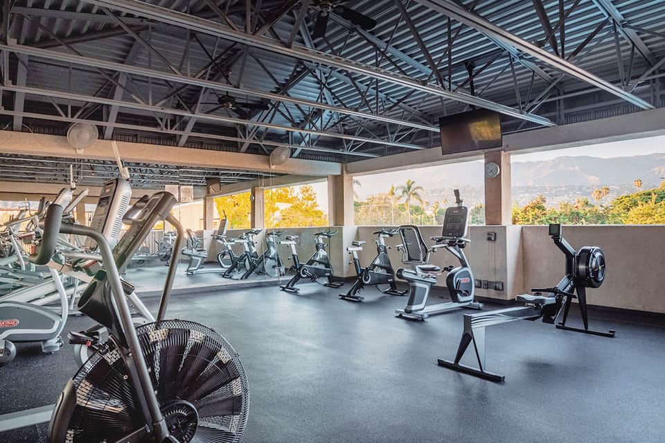 Rooftop fitness center with various exercise equipment and mountain landscape views through open sides