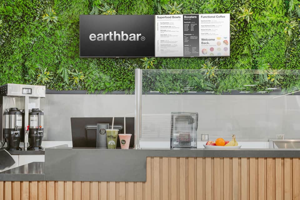 Earthbar café counter with green living wall backdrop and menu display