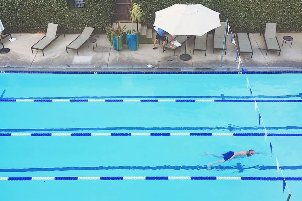 Competitive swimming pool with lap lanes, spectator seating, and white umbrella shade structure