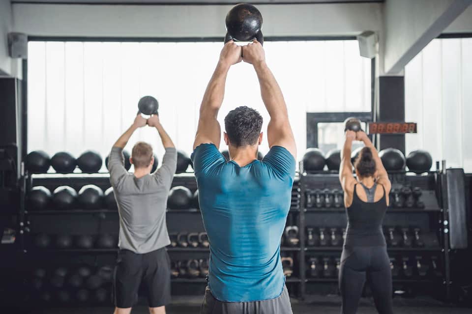 Fitness class with people performing kettlebell exercises in bright gym