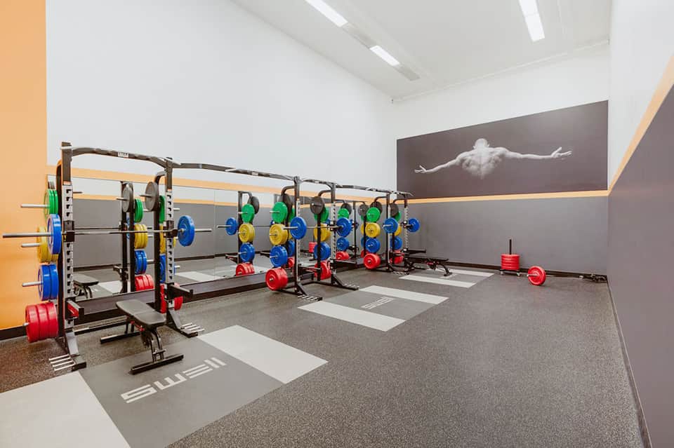 Modern fitness center with multiple barbell racks loaded with colorful weights and motivational wall art