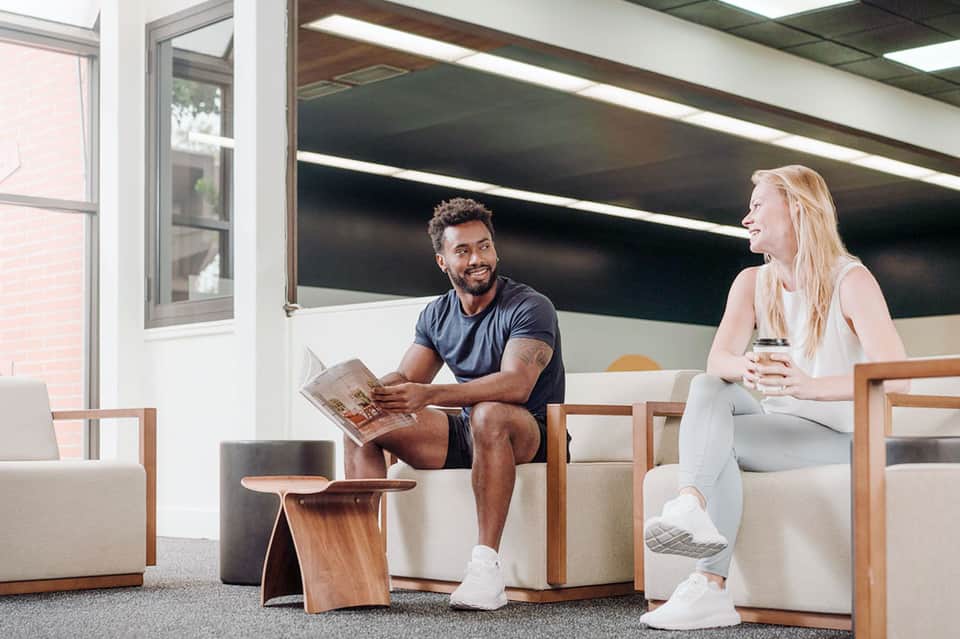 Two people chatting in modern lounge area with wooden furniture and large windows