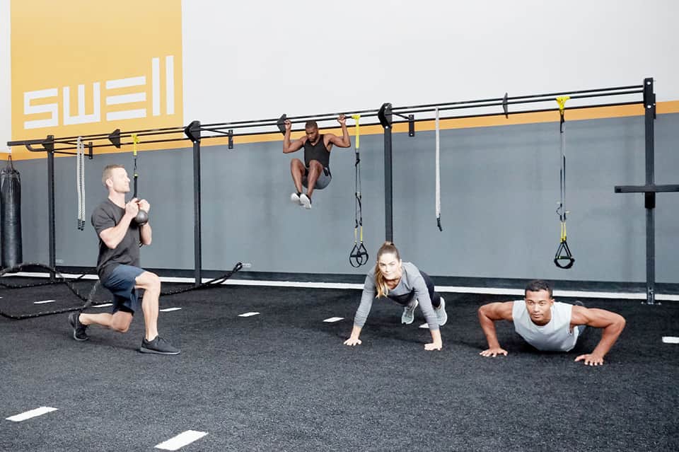 Group fitness class exercising under suspended rig with kettlebells and pull-up bars in modern gym