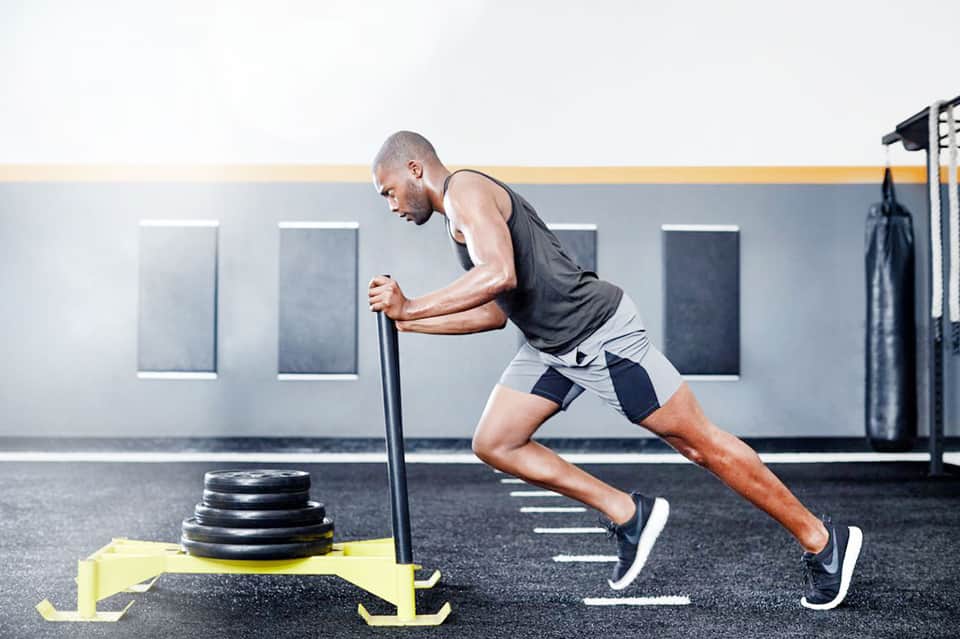 Man performing sled push exercise with weighted plates at a modern gym
