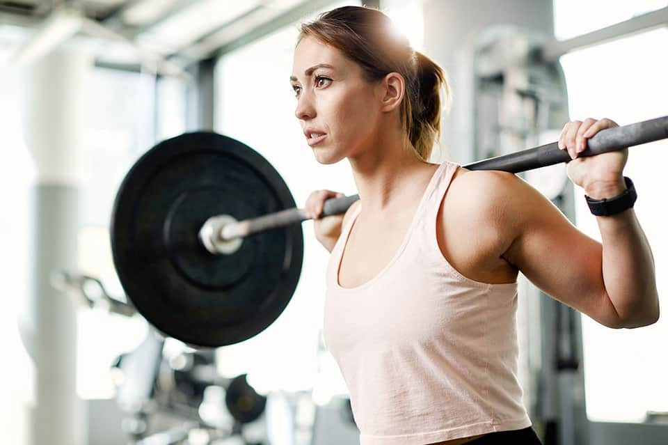 Athletic woman performing barbell squat exercise in bright, modern fitness gym