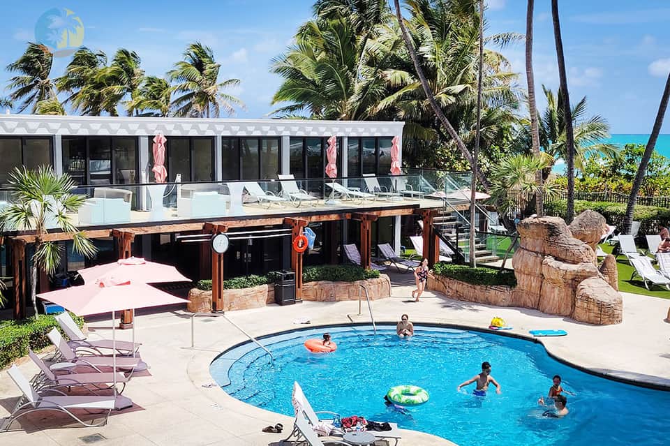 Family-friendly resort pool with water slide, palm trees, lounge chairs, and tropical setting