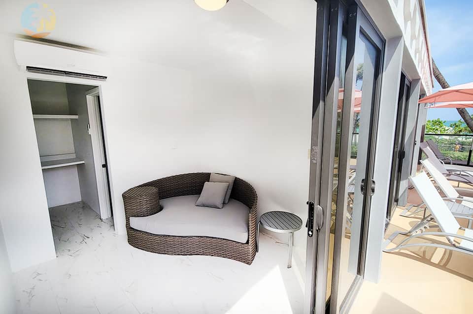 Modern white bedroom with woven daybed, shelving unit, and glass doors opening to outdoor terrace