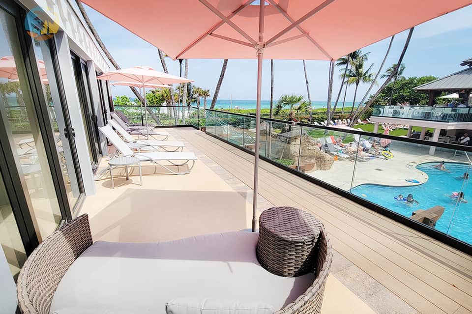 Oceanfront terrace with pink umbrellas, wicker seating, and pool overlooking tropical landscape