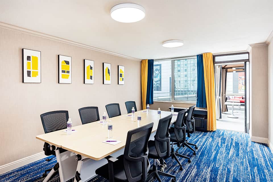 Modern conference room with long white table, black mesh chairs, blue curtains, and city views