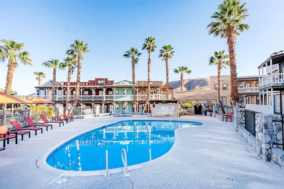 Resort pool with curved design, palm trees, western-style buildings, and desert mountain backdrop