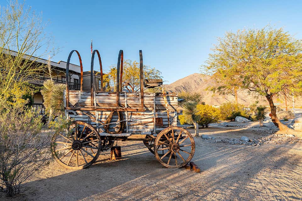 Rustic wooden wagon with metal wheels displayed in desert landscape with golden shrubs and hills