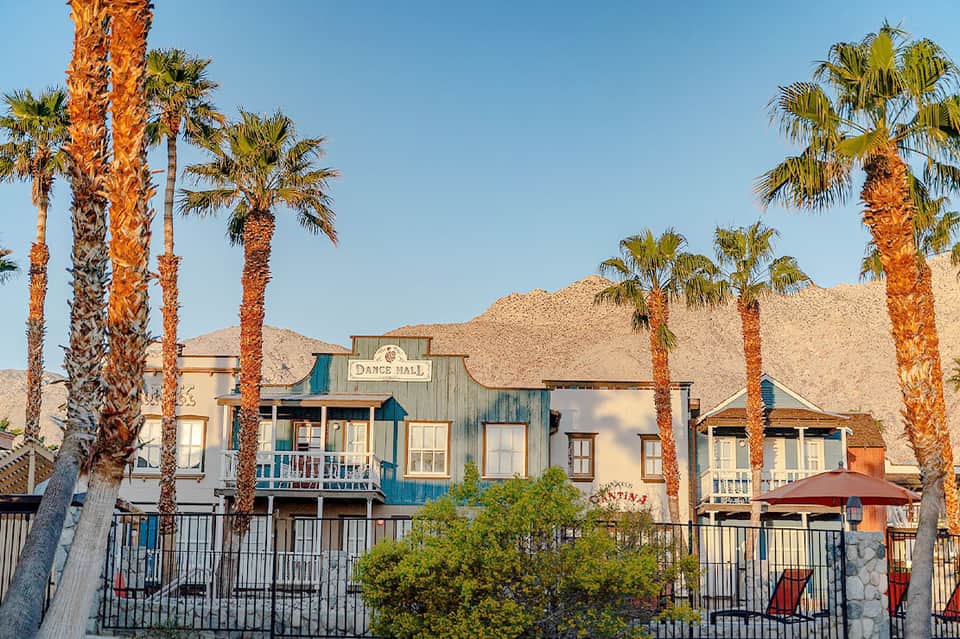 Western-style dance hall building with blue trim surrounded by palm trees and sandy hills