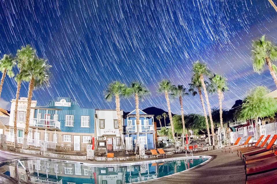 Vintage beach boardwalk with colorful beach houses, palm trees, and star-trail sky photography effect