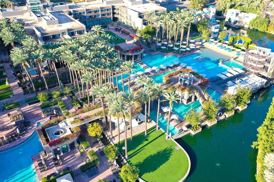 Aerial view of sprawling resort complex with multiple pools, palm trees, waterfront, and modern buildings