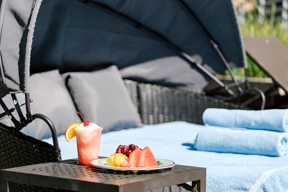 Tropical cocktail with fruit plate on table beside lounge chair with umbrella