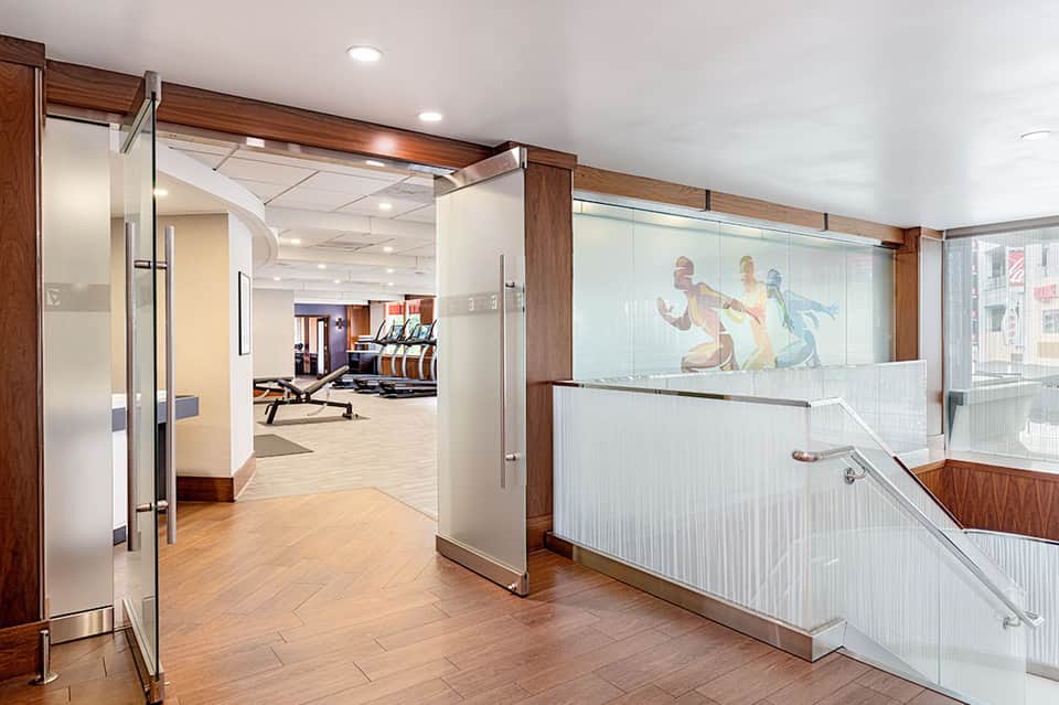 Modern fitness center entrance with glass doors, wooden framing, and gym equipment visible through windows