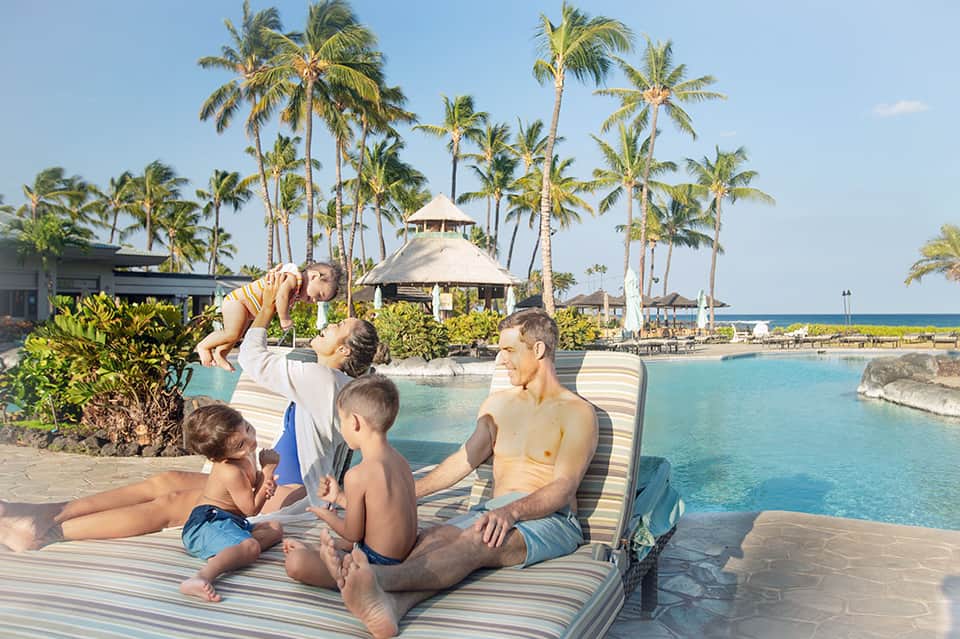 Family relaxing poolside with tropical palm trees and ocean view