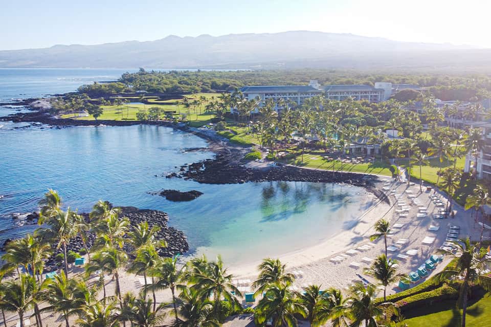 Aerial view of tropical beach resort with white sand, palm trees, and coastal mountains