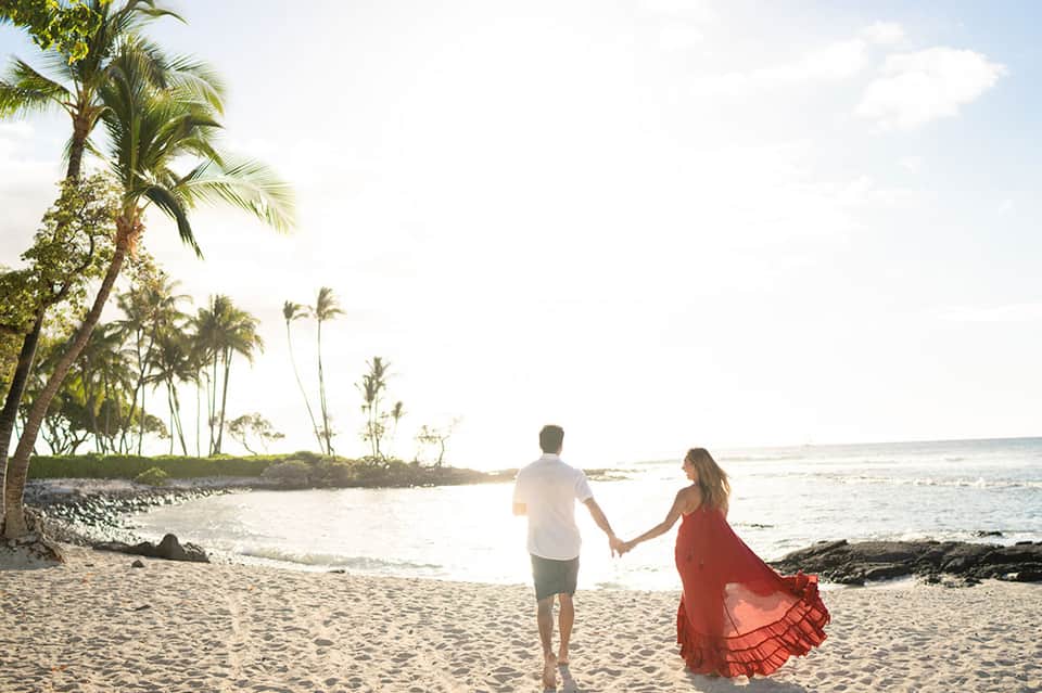 Couple holding hands on sandy beach with palm trees and ocean