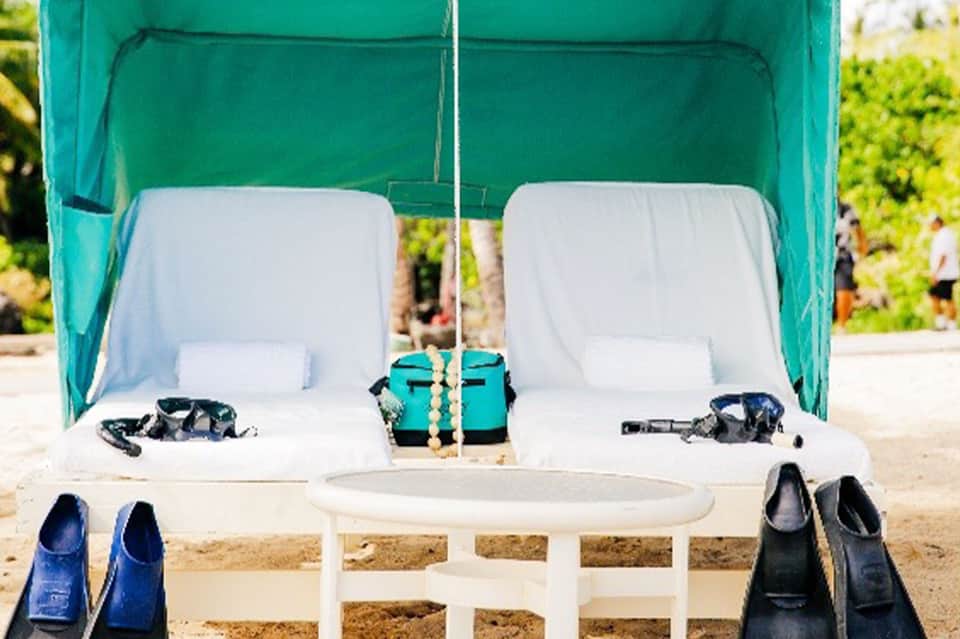 Beach cabana with turquoise canopy, white loungers, snorkel gear, and sand floor setup