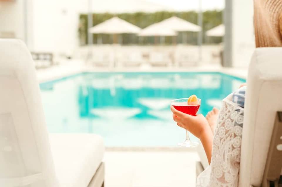 Guest holding colorful cocktail while overlooking turquoise pool and white umbrellas