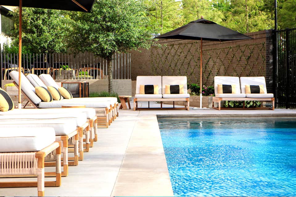 Luxury poolside lounge with white cushioned seating, black umbrella, and stone deck by pool