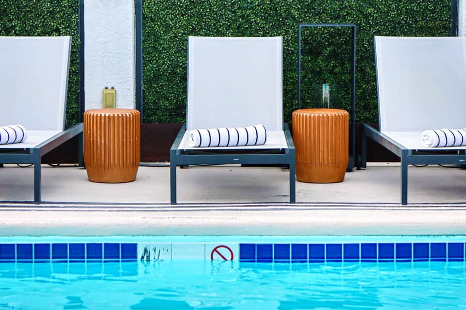 Poolside lounge chairs with striped cushions beside green living wall backdrop
