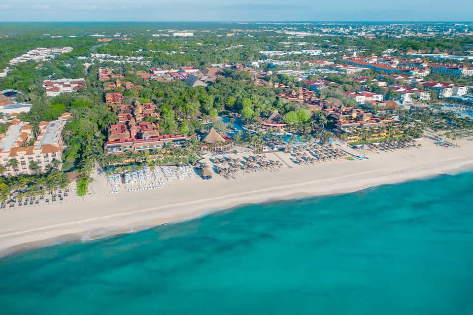 Aerial view of beachfront resort with sandy beach, palm trees, and turquoise water