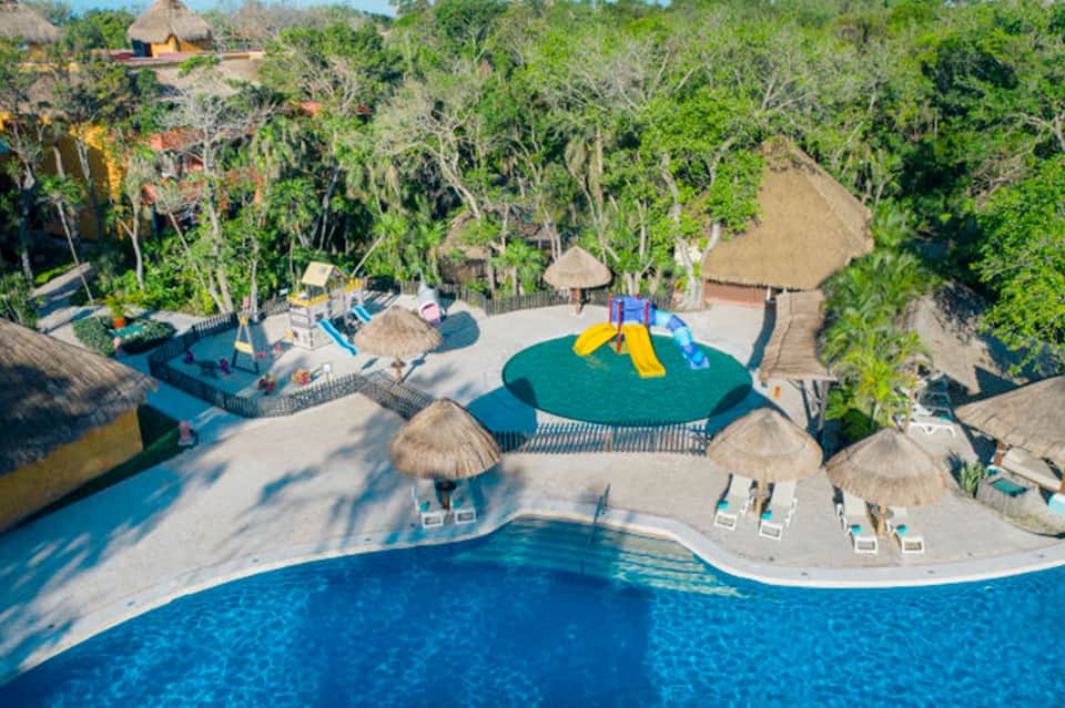 Aerial view of tropical resort with turquoise pools, thatched umbrellas, and jungle surroundings