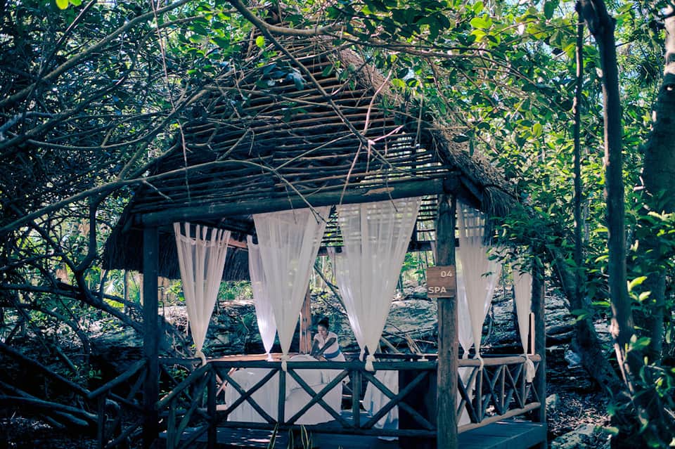 Wooden spa pavilion with white curtains nestled among lush green trees and foliage